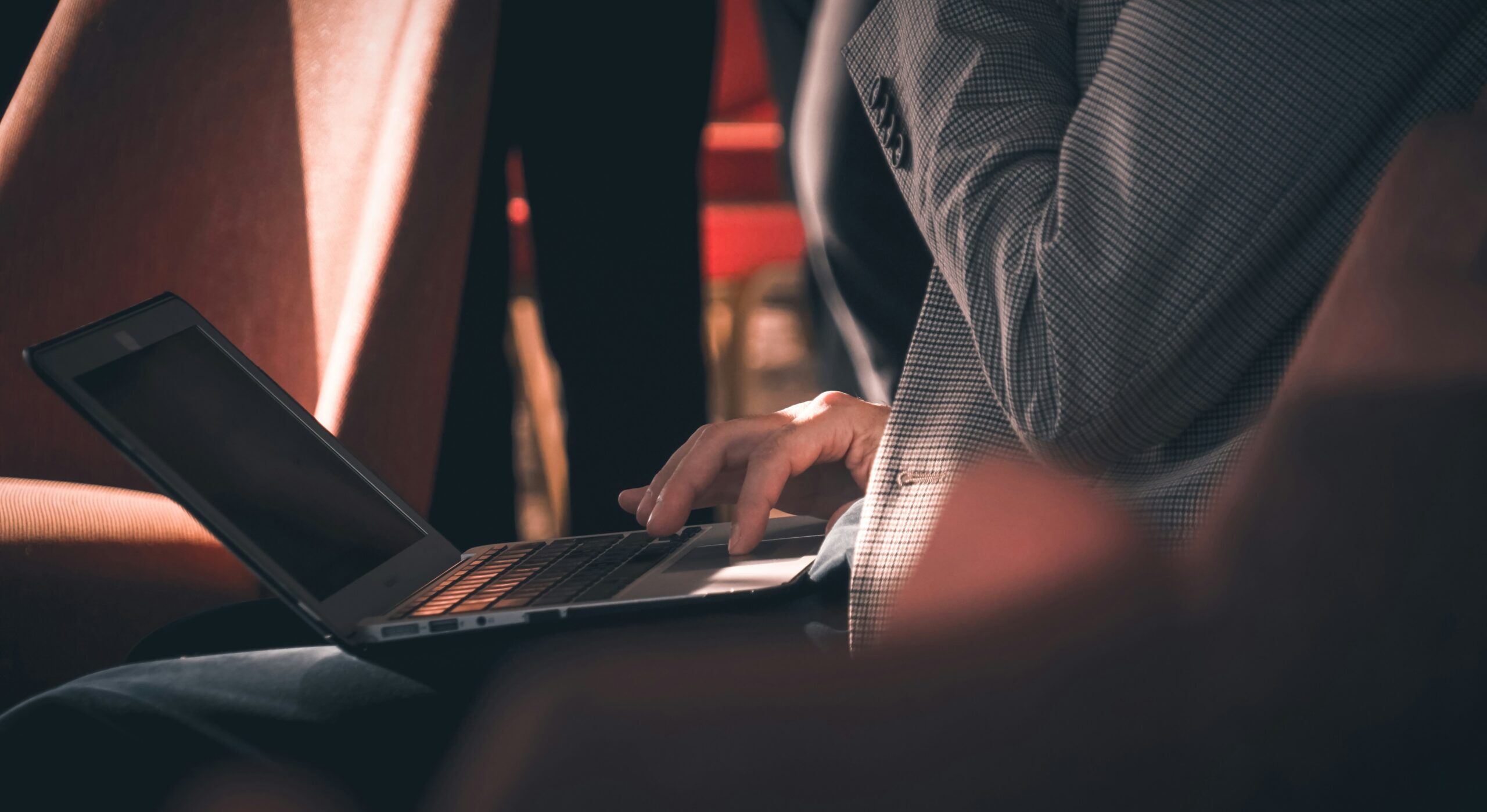 A person filling out paperwork at a desk with a laptop open